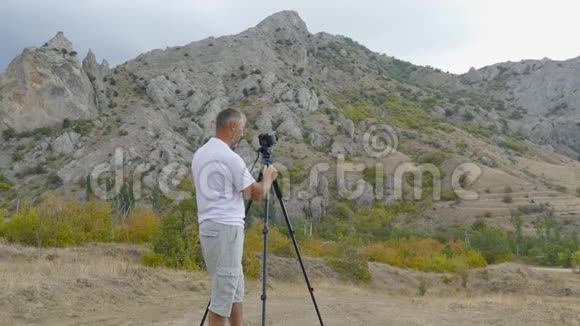 录像员用三脚架上的摄像机拍摄山脉视频的预览图