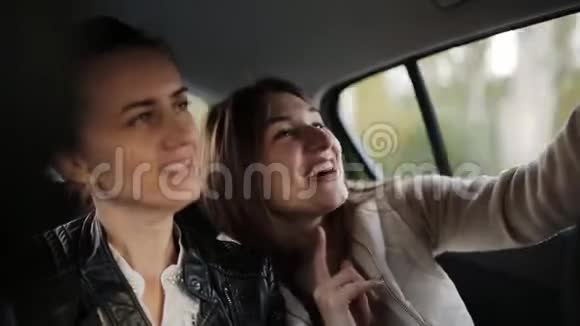 两个女人坐在坐出租车的汽车后座说话和使用智能手机视频的预览图
