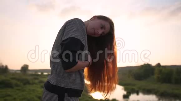 那个漂亮的女孩在日落时缓慢地在大自然上梳着长长的红色头发视频的预览图