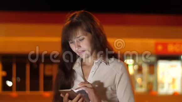 年轻女子晚上在停车场的智能手机上用灯笼说话很漂亮的女孩在打电话视频的预览图