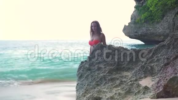 迷人的女人走在岩石海滩和海浪背景热带夏季海滩上穿泳衣的漂亮女人视频的预览图