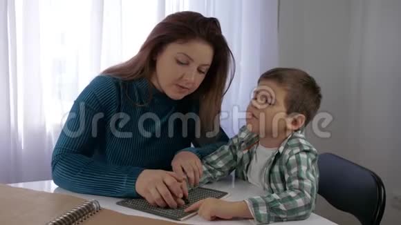 教育视力障碍儿童妈妈教盲儿男孩写盲文字体坐在桌子旁视频的预览图
