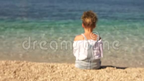 动态视频镜头接近坐在美丽清澈大海岸边的女孩女学生转身视频的预览图