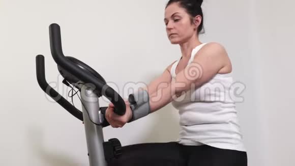 骑着运动自行车的女人完成锻炼并检查血压视频的预览图