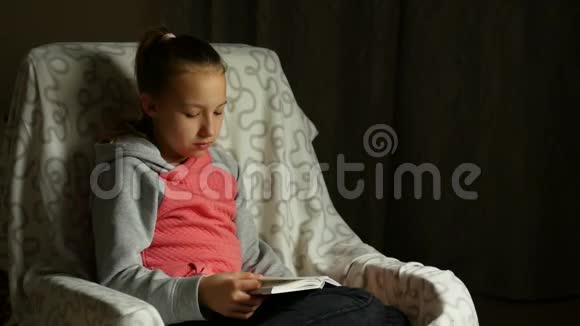 穿灰色粉红色运动衫的可爱的女孩子坐在房间里舒适的椅子上看书视频的预览图