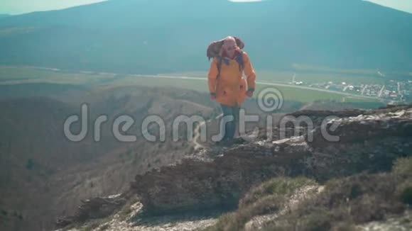一个穿着黄色夹克眼镜和一个大型旅游背包的人沿着山脊散步欣赏风景视频的预览图
