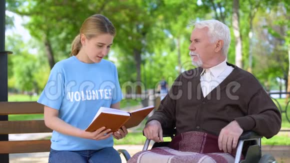 年轻女性志愿者为坐轮椅的残疾养老金领取者阅读书籍视频的预览图