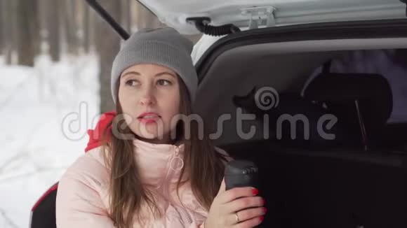 阳光明媚的冬日美丽的女孩坐在车上喝着小热水瓶里的茶视频的预览图