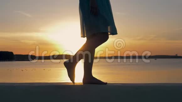 在夕阳下闪闪发光的沙滩上女子双脚的特写视频的预览图