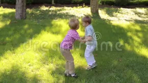 两个快乐的小男孩玩得很开心在公园的草地上跳视频的预览图