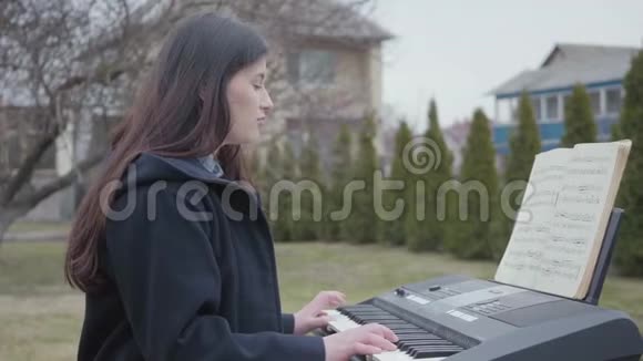 一个美丽的黑发女孩在一个合成器上玩耍在户外坐在后院唱歌成功的青年视频的预览图
