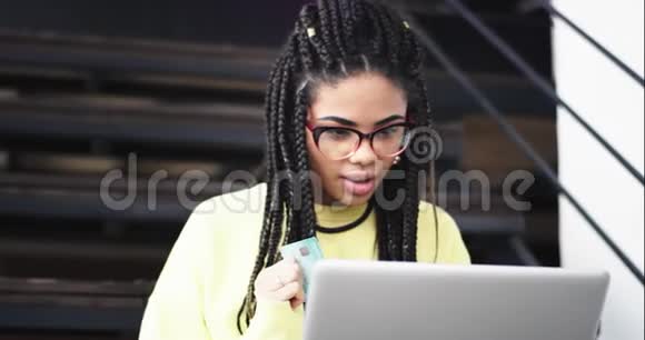 漂亮的非洲女士用她的银行卡用她的笔记本电脑检查或网上买东西她穿着视频的预览图
