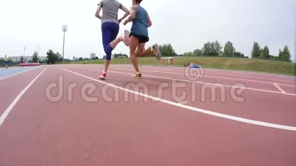 在一天的慢动作训练中年轻男女运动员在田径跑道上的镜头前奔跑视频的预览图