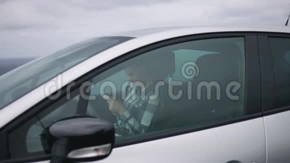 女孩坐在车里拿着智能手机在大海的背景下笑着视频的预览图