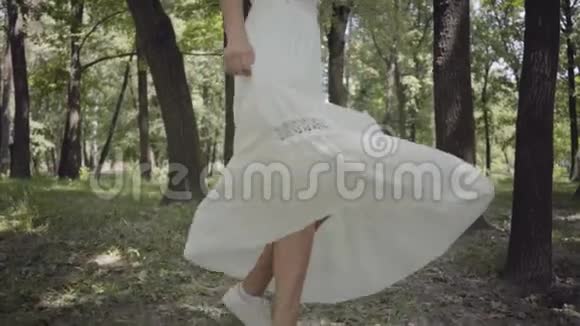 不认识的女孩穿着白色的长夏礼服在公园里旋转一个漂亮女人在户外休闲慢慢视频的预览图