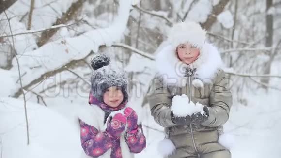 冬季森林两个快乐的小女孩站在彼此旁边把雪扔了起来视频的预览图