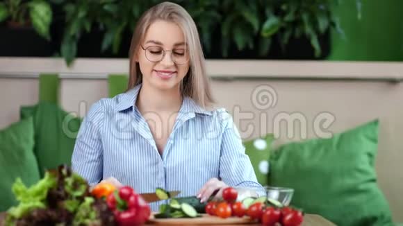 微笑的年轻女子切新鲜黄瓜烹饪食物沙拉在厨房中等特写视频的预览图