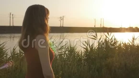 日落时分带着芦苇沿着河岸散步的美丽女孩的剪影轮廓夏天可爱的女人在大自然中漫步罗马视频的预览图