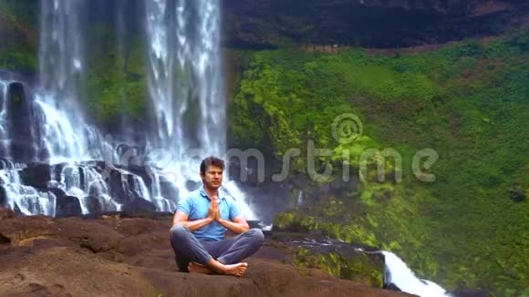 强壮的男人坐在瀑布的岩石上的普拉纳亚瑜伽姿势视频的预览图