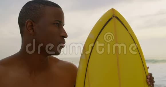 非裔美国男性冲浪者站在海滩上冲浪板的正面景色视频的预览图