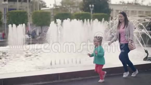 在城市公园的喷泉背景下嬉戏玩耍的小女孩和妈妈视频的预览图