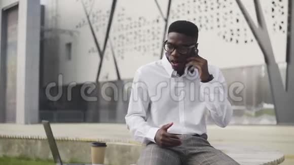 戴眼镜的严肃非洲商人在城市公园用手机说话视频的预览图