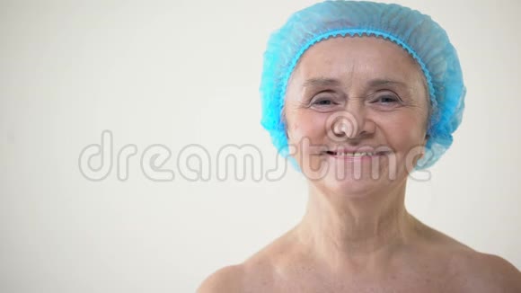 戴着保护帽微笑的老年女性看着摄像机整容手术视频的预览图