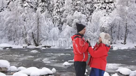 恋爱中的情侣在一条山河附近的冬日森林里谈情说爱视频的预览图