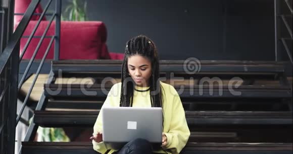 漂亮的上班族年轻的非洲裔女士在一个现代化的办公室大厅里工作坐在楼梯上打字视频的预览图