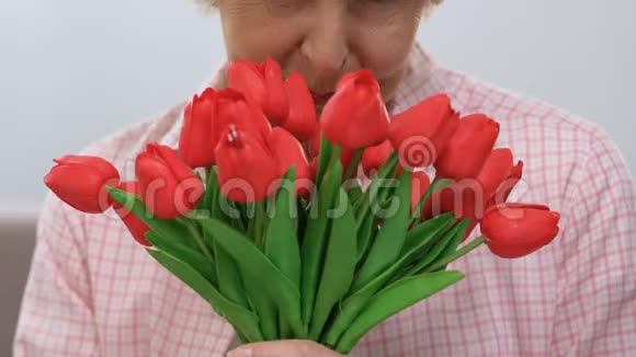 美丽的老妇人嗅着一束郁金香对着镜头微笑节日视频的预览图