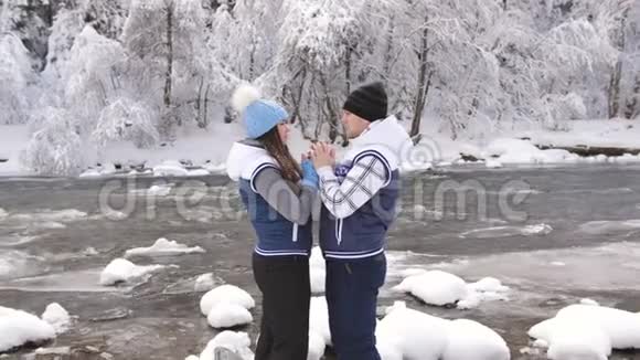 恋爱中的情侣在一条奔腾的山河的河岸上在冬日的森林里欢笑和拥抱视频的预览图