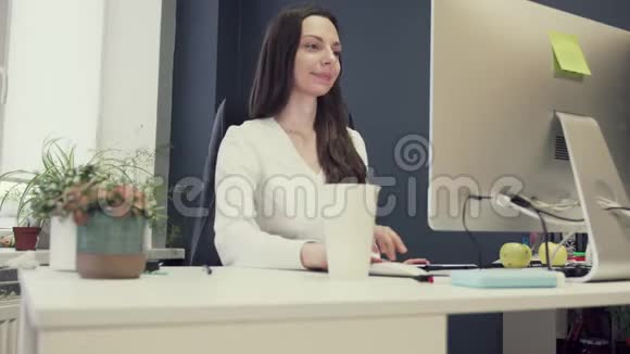 一位有创造力的女人坐在办公桌前用电脑快乐地在创意办公室工作视频的预览图