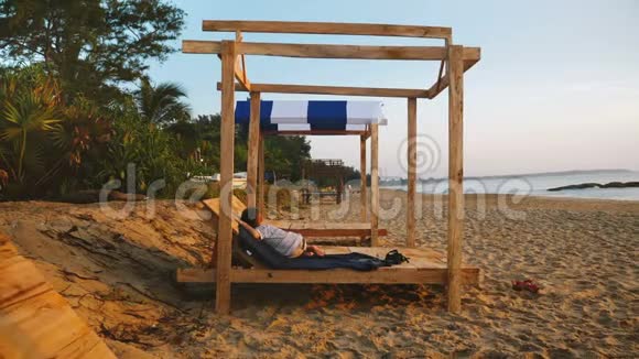 美丽的照片快乐的小男孩放松的孩子睡在海滩躺椅附近日落海浪在异国情调的海岸视频的预览图