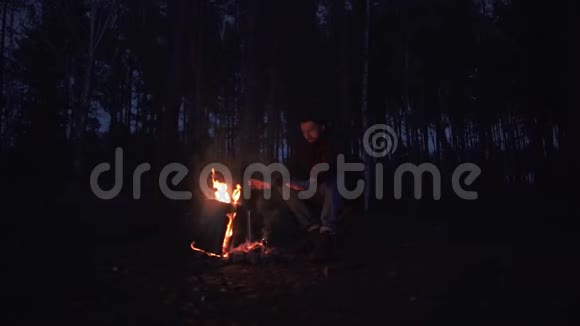 一个留胡子的年轻人坐在椅子上在炉火旁温暖着他的手森林里的火堆旁一个残忍的家伙视频的预览图