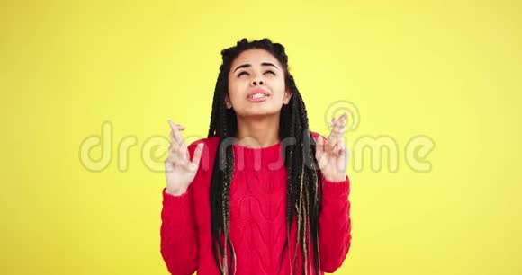在一个有着黄色背景的工作室里一位富有魅力的风趣幽默的非洲多民族女士一位交叉着手指和恐惧的人视频的预览图