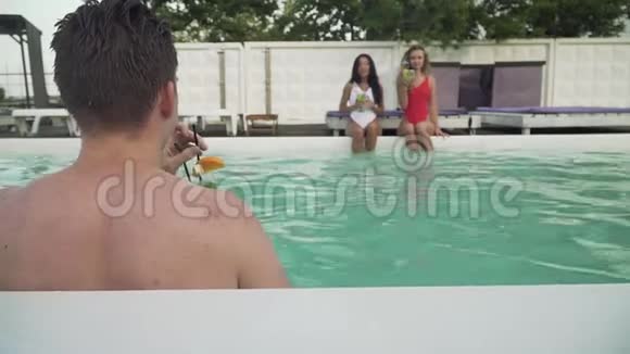 在两个漂亮女孩的背景下湿漉漉的年轻人从露天游泳池出来A视频的预览图
