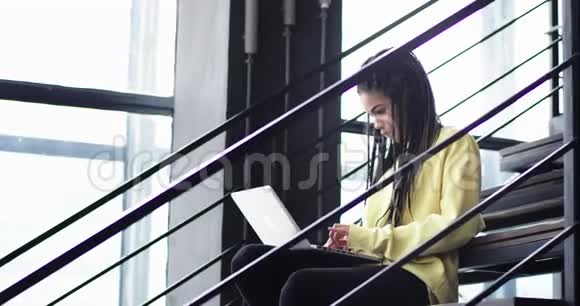在一座现代化的办公楼里有一扇大窗户漂亮的非洲女性在笔记本上工作坐在上面视频的预览图