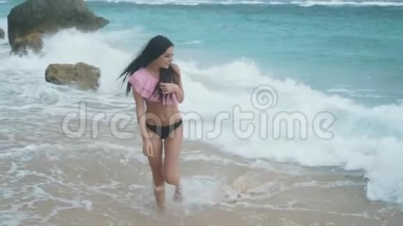慢动作运动的快乐女孩穿着泳装在海浪中沿着海滩散步Stealicam射击视频的预览图