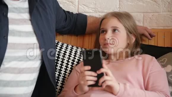 年轻的父亲和女儿一起在咖啡馆喝茶女孩拿着她的智能手机视频的预览图