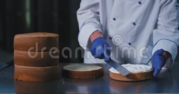 一双蓝色手套的特写手里拿着一把铲子优雅地把奶油撒在蛋糕上看上去很漂亮视频的预览图