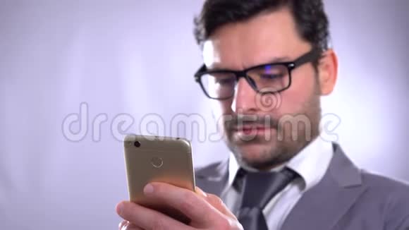 一个年轻人在灰色背景下使用手机的4K视频片段一直保持联系微笑的年轻人抱着视频的预览图
