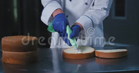 一个年轻人穿着整洁干净的蓝扣面包师制服在蛋糕的下半部分涂上糖霜视频的预览图