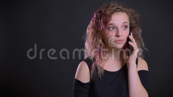 年轻的白种人女孩的肖像粉红色的头发愉快地在黑色背景下的手机上交谈视频的预览图