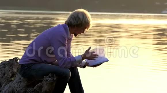 金发男人在湖边读一只靴子写一篇文章视频的预览图