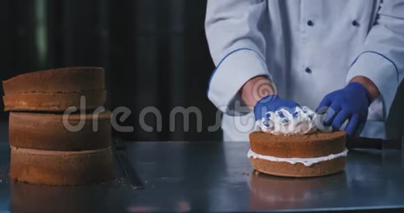 一个带着蓝色橡胶手套的胖乎乎的手的面包师正用手把这种丝滑的白色奶油撒在蛋糕上视频的预览图