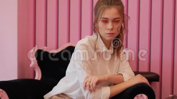 年轻模特在粉色工作室的椅子上摆姿势视频的预览图