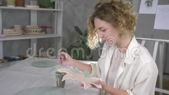令人鼓舞的手工制作主人幸福的女人用刷子在陶瓷上用绿色油漆装饰新制作的陶盘视频的预览图