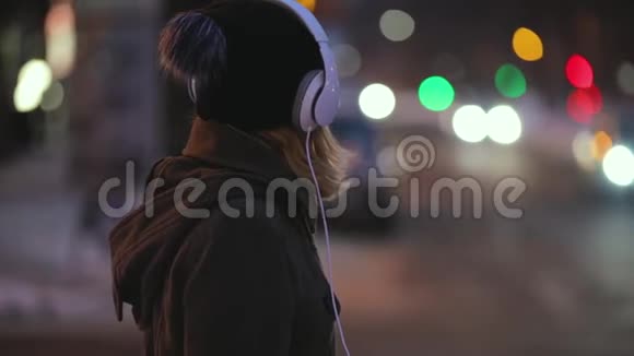 戴着耳机的独身女子准备过马路城市之夜视频的预览图