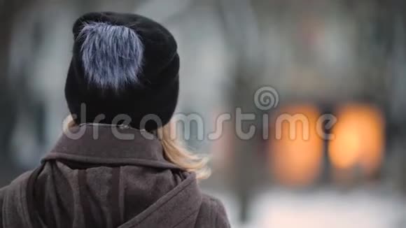 在冬季傍晚城市用耳机听音乐的无法辨认的女人的后景视频的预览图