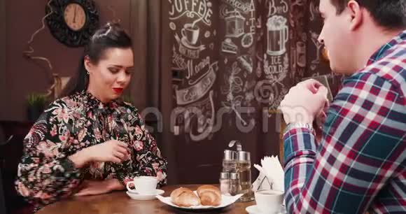 在时尚时髦的时髦咖啡店酒吧餐厅喝咖啡和吃羊角面包的情侣视频的预览图